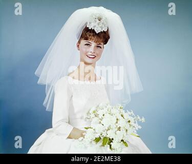 1960s SMILING BRUNETTE BRIDE PORTRAIT IN SIMPLE WHITE WEDDING GOWN HOLDING WHITE FLOWER BOUQUET WEARING VEIL LOOKING AT CAMERA - kb5239 HAR001 HARS BEAUTIFUL CELEBRATION FEMALES MARRIED STUDIO SHOT EVENT GROWNUP COPY SPACE HALF-LENGTH LADIES MARRIAGE PERSONS GROWN-UP VEIL CEREMONY BRIDAL EYE CONTACT BRUNETTE PEOPLE STORY DREAMS HAPPINESS CHEERFUL BRIDES CUSTOM EXCITEMENT TRADITION NUPTIAL NUPTIALS OCCASION MARRYING PRIDE SIMPLE SMILES JOYFUL RITE RITE OF PASSAGE STYLISH WED FACIAL EXPRESSION MARRY MATRIMONY WEDLOCK YOUNG ADULT WOMAN BANGS CAUCASIAN ETHNICITY HAR001 OLD FASHIONED Stock Photo