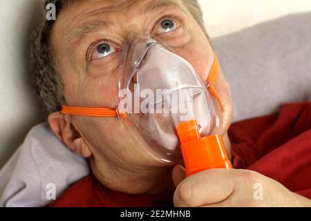 Sick senior adult man breathing through oxygen mask, rolling his eyes. Treatment of asthma, allergies, bronchitis, pneumonia in Covid-19 and respirato Stock Photo