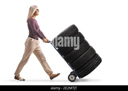 Full length profile shot of a young woman pushing a hand-truck loaded with car tires isolated on white background Stock Photo