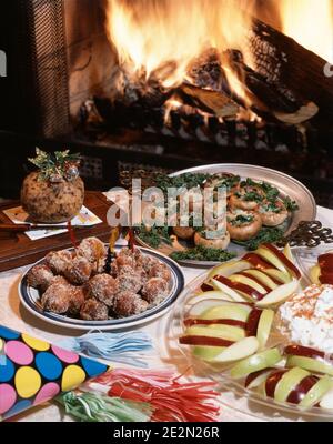 1980s CHRISTMAS PARTY FOODS FRUIT STUFFED MUSHROOMS CHEESE BALL RUM BALLS FIREPLACE IN BACKGROUND - kx9993 DAS001 HARS OLD FASHIONED Stock Photo