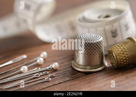 Sewing items - thimbles, including pins, measuring tape on background. Stock Photo