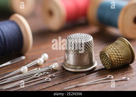 Two thimbles and including pins. Various wooden spools of multicolored threads on background.