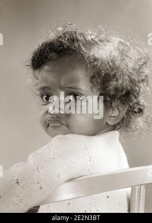 1940s 1950s AFRICAN AMERICAN BABY GIRL SITTING UP IN CHAIR LOOKING OVER HER SHOULDER BIG EYES UNRULY CURLY HAIR - n324 HAR001 HARS B&W POUTING AFRICAN-AMERICANS AFRICAN-AMERICAN BLACK ETHNICITY CURLY IN UP POUT JUVENILES BABY GIRL BLACK AND WHITE HAR001 OLD FASHIONED AFRICAN AMERICANS Stock Photo