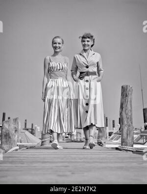 1940s 1950s TWO SMILING YOUNG WOMEN WEARING STYLISH SUMMER DRESSES WALKING SIDE-BY-SIDE ON WOODEN BOAT DOCK AT A MARINA  - y736 HAR001 HARS YOUNG ADULT TEAMWORK VACATION BUTTONS PLEASED JOY LIFESTYLE SATISFACTION FEMALES BOATS HEALTHINESS COPY SPACE FRIENDSHIP FULL-LENGTH LADIES PERSONS DOCK STRIPES SIBLINGS CONFIDENCE SISTERS TRANSPORTATION B&W SUMMERTIME EYE CONTACT DRESSES TIME OFF HAPPINESS CHEERFUL ADVENTURE LEISURE STYLES TRIP GETAWAY LOW ANGLE RECREATION PRIDE A AT ON HOLIDAYS SIBLING SMILES CONNECTION BOATING FRIENDLY JOYFUL STYLISH SUN DRESS COOPERATION FASHIONS SEASON SIDE-BY-SIDE Stock Photo