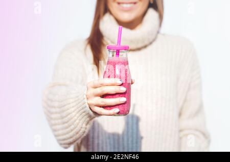 Smiling woman in woollen sweater holding bottle with pink homemade detox blueberry and raspberry smoothie or juice. Healthy clean eating Stock Photo