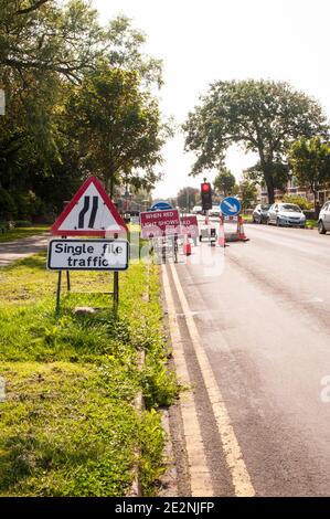 Road works traffic warning & lane indicator signs with single lane traffic controlled by traffic lights on red Road narrows on left & keep right signs Stock Photo