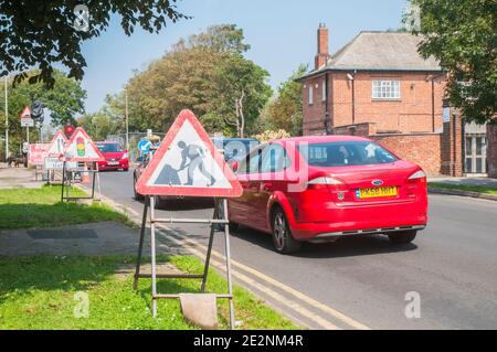 Cars waiting at road works with traffic warning & lane indicator signs with single lane traffic controlled by traffic lights on red Stock Photo