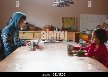 A father working on computer and child eating breakfast sit together Stock Photo