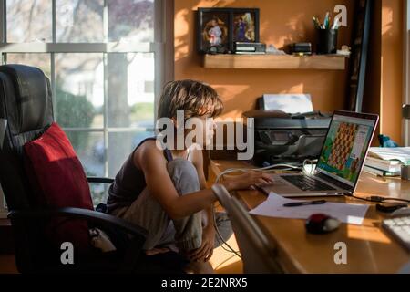 A preteen boy sits at computer playing an online chess game at desk Stock Photo