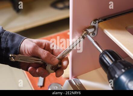 Carpenter working on play furniture. Fixing closers on play kitchen oven door with screwdriver close up Stock Photo