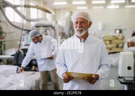 Father and son checking products in their food factory. Mature man in sterile clothes standing in front of the camera with smile on his face.Successfu Stock Photo