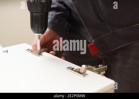 Carpenter at work. Fixing door hinge with electric screwdriver closeup Stock Photo
