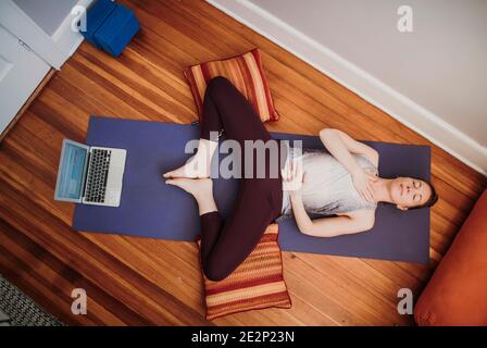 Woman in athletic wear with laptop computer relaxes on floor of home Stock Photo