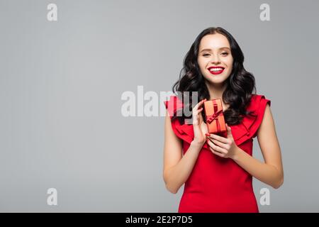 cheerful woman in ruffled dress pulling ribbon on gift box isolated on ...