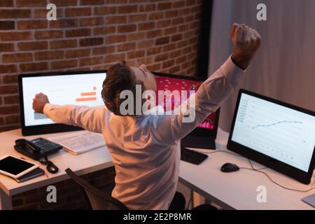 Businessman stretching near computers with charts on blurred background at evening Stock Photo