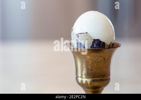 Hard boiled Quail egg in brass egg holder with shell cracked open ready to be eaten Stock Photo
