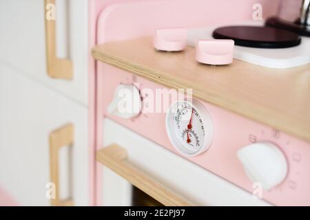 Stylish wooden furniture for children. Thermometer and knobs on pink play kitchen closeup Stock Photo