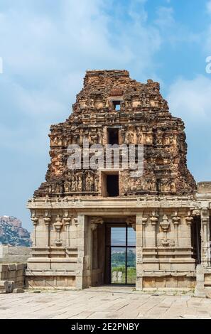 Hampi, Karnataka, India - November 5, 2013: Vijaya Vitthala Temple. Entrance and ruinous Gopuram under blue cloudscape. Remains of statues and some gr Stock Photo