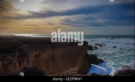 people walking on a clifftop coastal path at sunset with Big waves crashing along the coast in Montaña de Oro State Park, Central California, USA Stock Photo