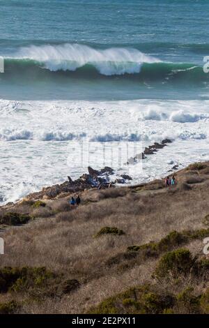 people walking on a coastal path with Big waves crashing along the coast in Montaña de Oro State Park, Central California, USA Stock Photo