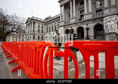 Capitol Police stand guard behind orange barricades at the Pennsylvania Capitol.An FBI bulletin warned that armed protests were planned at all the 50 state capitols in the days leading up to President-elect Joe Biden's inauguration. Stock Photo