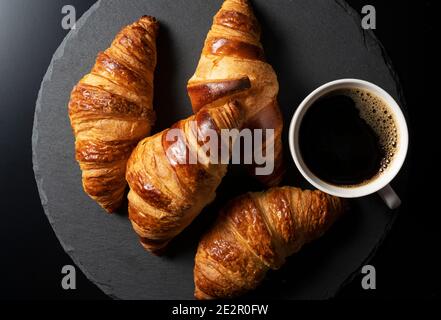 Croissants and hot coffee on a black stone plate with a black background. A view from above Stock Photo