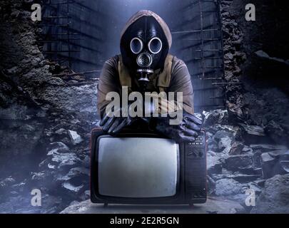 Photo of stalker soldier in jacket and armored vest and rubber gloves standing with old tv set on ruined dark background. Stock Photo