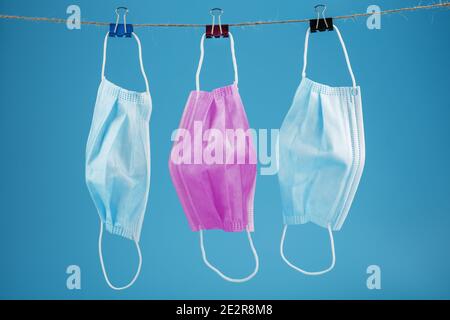 Three medical masks hanging on a rope, pink and blue on a blue background. The concept of Protection from the virus and colds Stock Photo