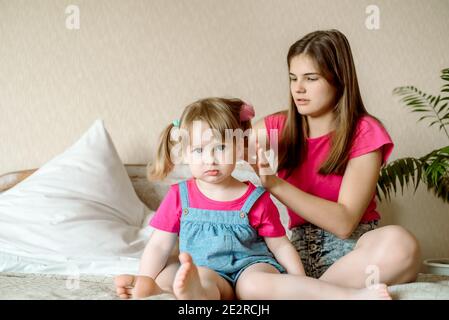 Children play on the bed in a bright bedroom. teen girl combing baby hair. funny girls. sisterly love. vacation home. Stock Photo