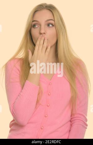 Studio shot of young beautiful teenage girl covering mouth while looking shocked Stock Photo