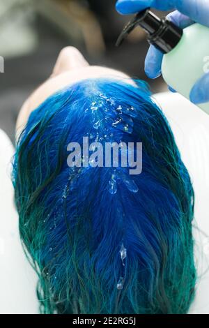 Professional hairdresser applies shampoo to client's blue hair for washing after process of coloring hair in dark blue color. Stock Photo