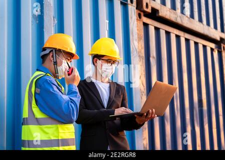 Teamwork, Asian male logistic warehouse foreman with worker using laptop checking list planning and strategy of container boxes from cargo freight shi Stock Photo