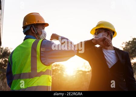 Asian industry construction site worker and foreman wearing hygiene face mask elbow bump greeting adaptation to prevent Coronavirus or Covid-19 spread Stock Photo