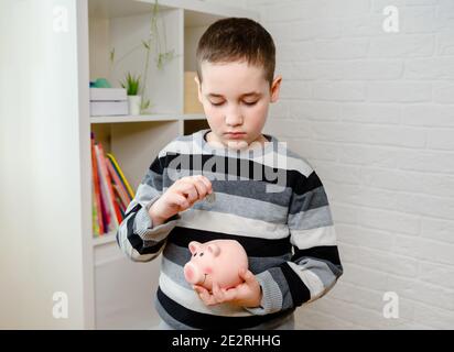 Boy putting coins into piggy bank. Learning financial responsibility  Stock Photo
