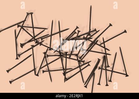 A bunch of self-tapping screws for wood surfaces on a beige background. Metal fasteners. Stock Photo