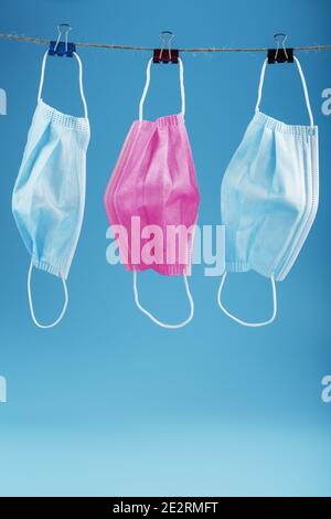 Three medical masks hanging on a rope, pink and blue on a blue background. The concept of Protection from the virus and colds Stock Photo