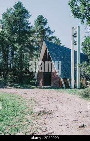 a church with nothing around in the middle of a hiking trail, surrounded by trees and bushes with two bells on one side of the building Stock Photo