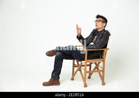 Man in a director's chair on a white background in the studio, a man in a black leather jacket, jeans and glasses. modern film art Stock Photo