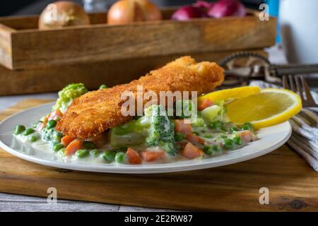 breaded fish with mixed vegetables in a creamy sauce Stock Photo
