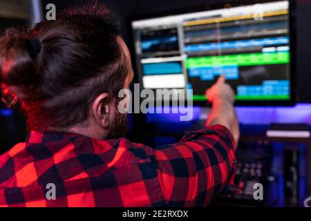 Young DJ man is showing on the computer in recording program what the idea he wants to add in his new song. Stock Photo