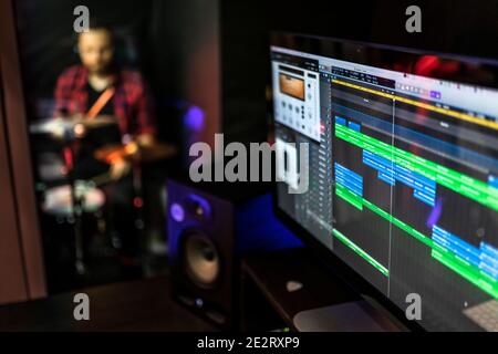 Sound program on the computer for DJ, songwriter, producer to create new ideas in the stereo studio while young man is playing drums. Stock Photo