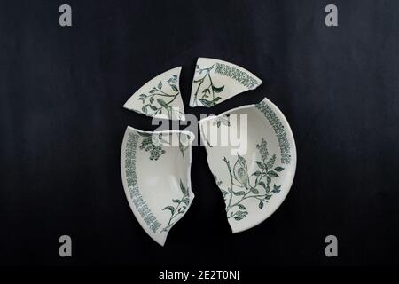 Broken plate on a black background. A deep pictured rarelka shattered into four fragments. Insulated porcelain old tableware. Stock Photo