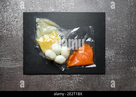 Products in vacuum packaging on black slate board. Boiled eggs and vegetables for making salad, vacuum sealed food ready for sous vide cooking. Sous-v Stock Photo