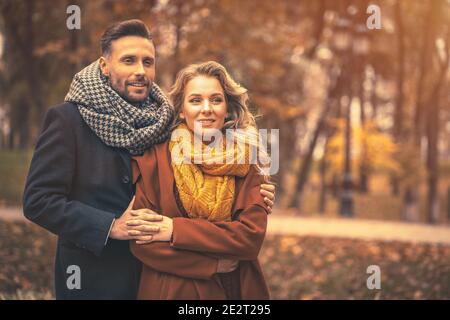 Couple in love man and a woman hugged from behind smile looking at their kids in the autumn park. Outdoor shot of a young couple in love having great Stock Photo