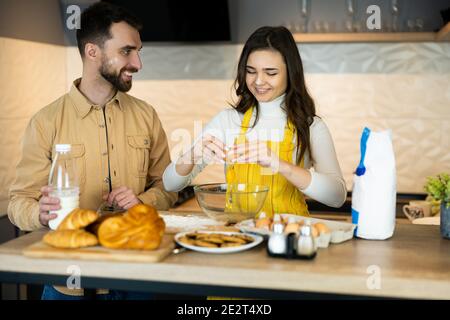Cute couple are spending time while cooking and seem happy being together in the kitchen. They are baking some cookies and buns. Stock Photo