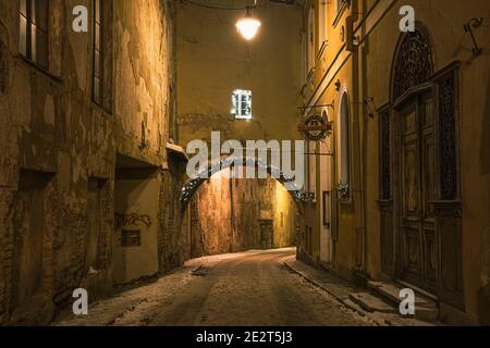 Beautiful narrow street of Vilnius Old Town, evening or night view with old buildings and street lamp in winter with snow Stock Photo