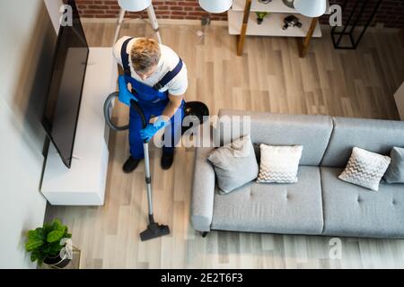 Man In Uniform Vacuuming House Floor. Cleaning Home Stock Photo