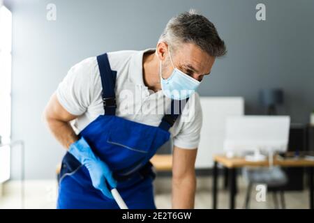 Male Janitor Mopping Floor In Face Mask In Office Stock Photo