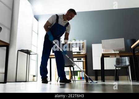 Male Janitor Mopping Floor In Face Mask In Office Stock Photo