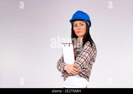 Serious female engineer with a folder in hands looking at the camera on a gray background with blank space. Stock Photo